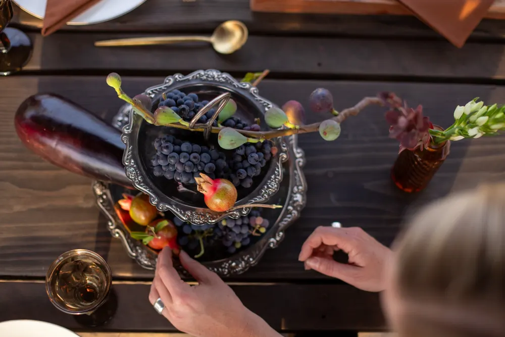 A pedestal bowl of plums and figs being arranged.