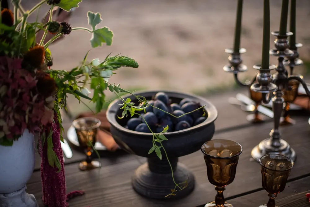 Candles, goblets and a bowl of plums.