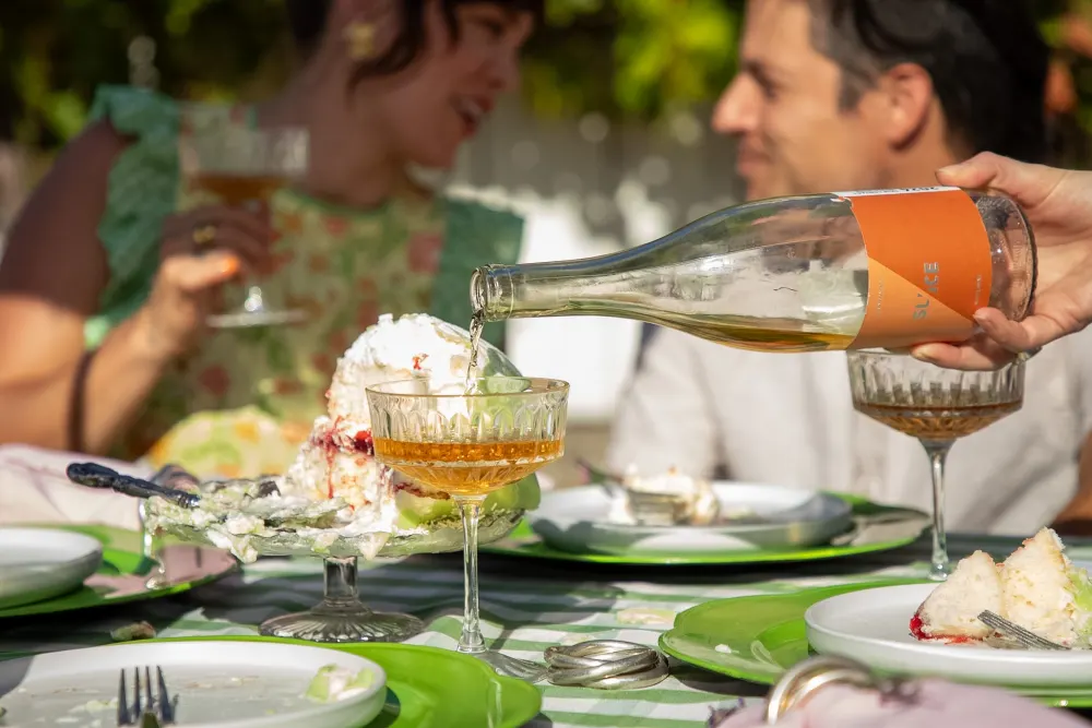 Pouring sparkling wine into coupes at a garden table.