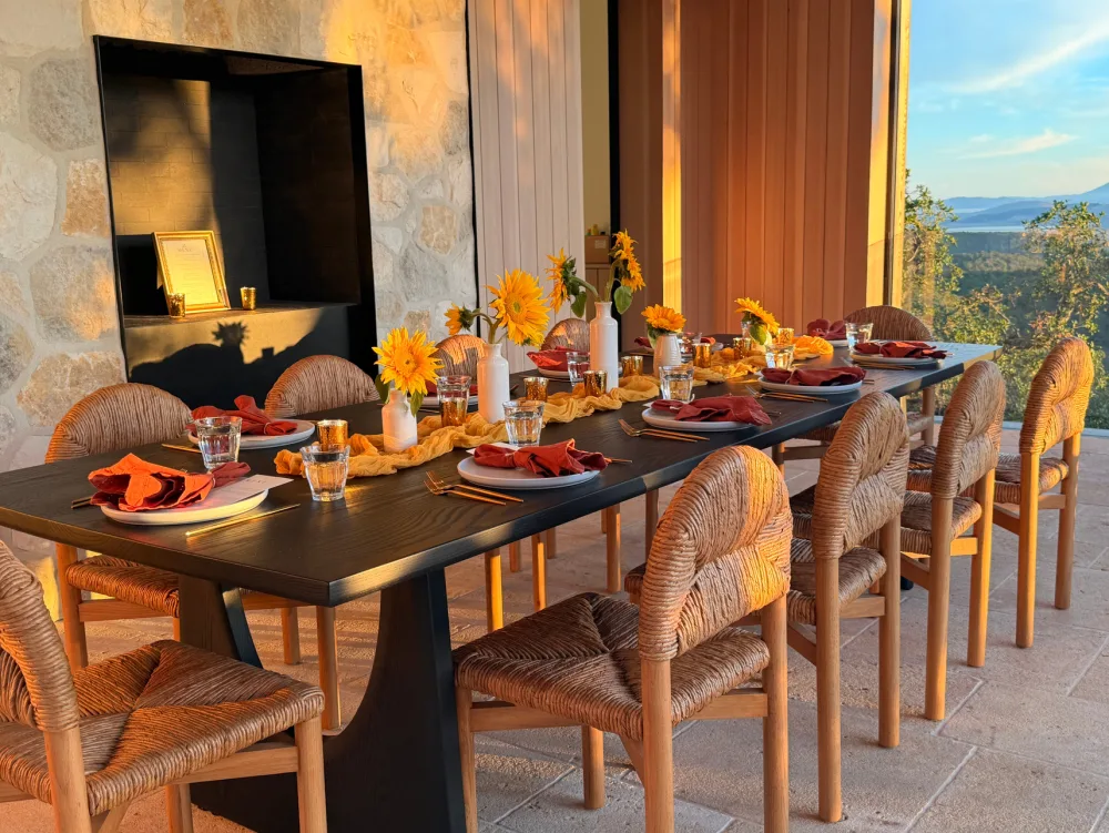 A long black table set with sunflowers beside a window onto the hills.