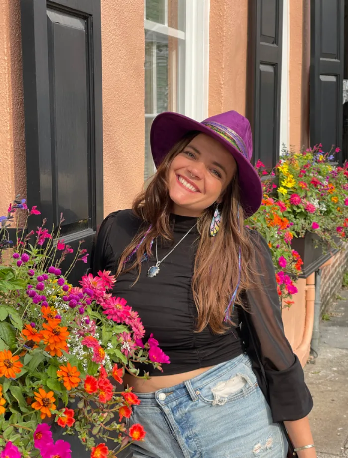 Hannah Lapolla in a purple hat beside a window box of flowers.