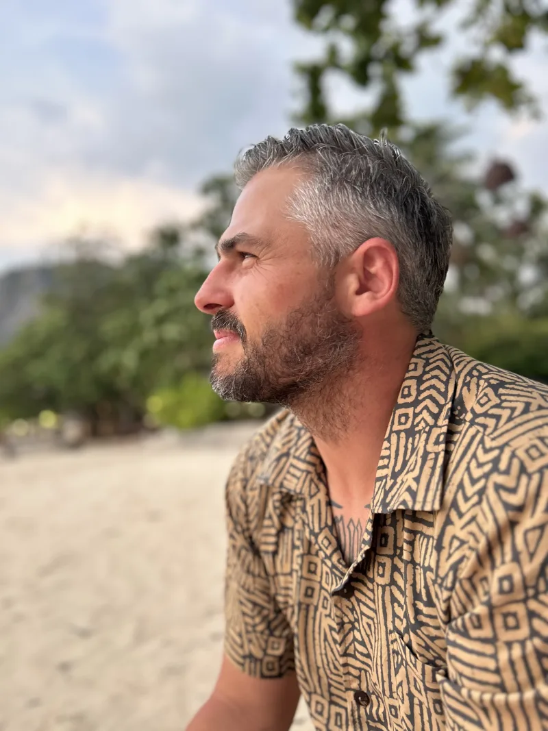 Luke Young in a patterned shirt on a beach at sunset.